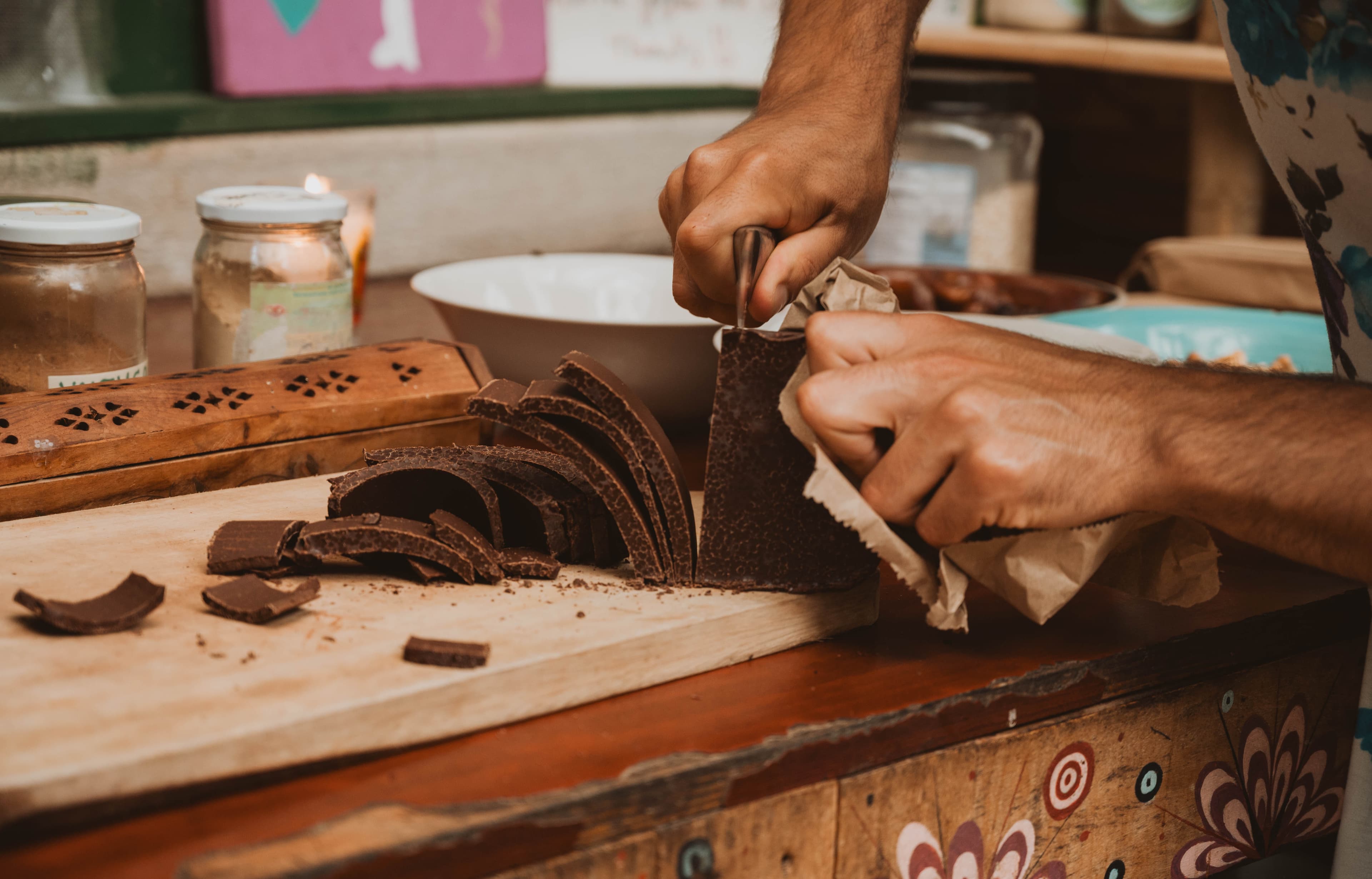 Hands shaving a block of ceremonial cacao on a painted wooden table