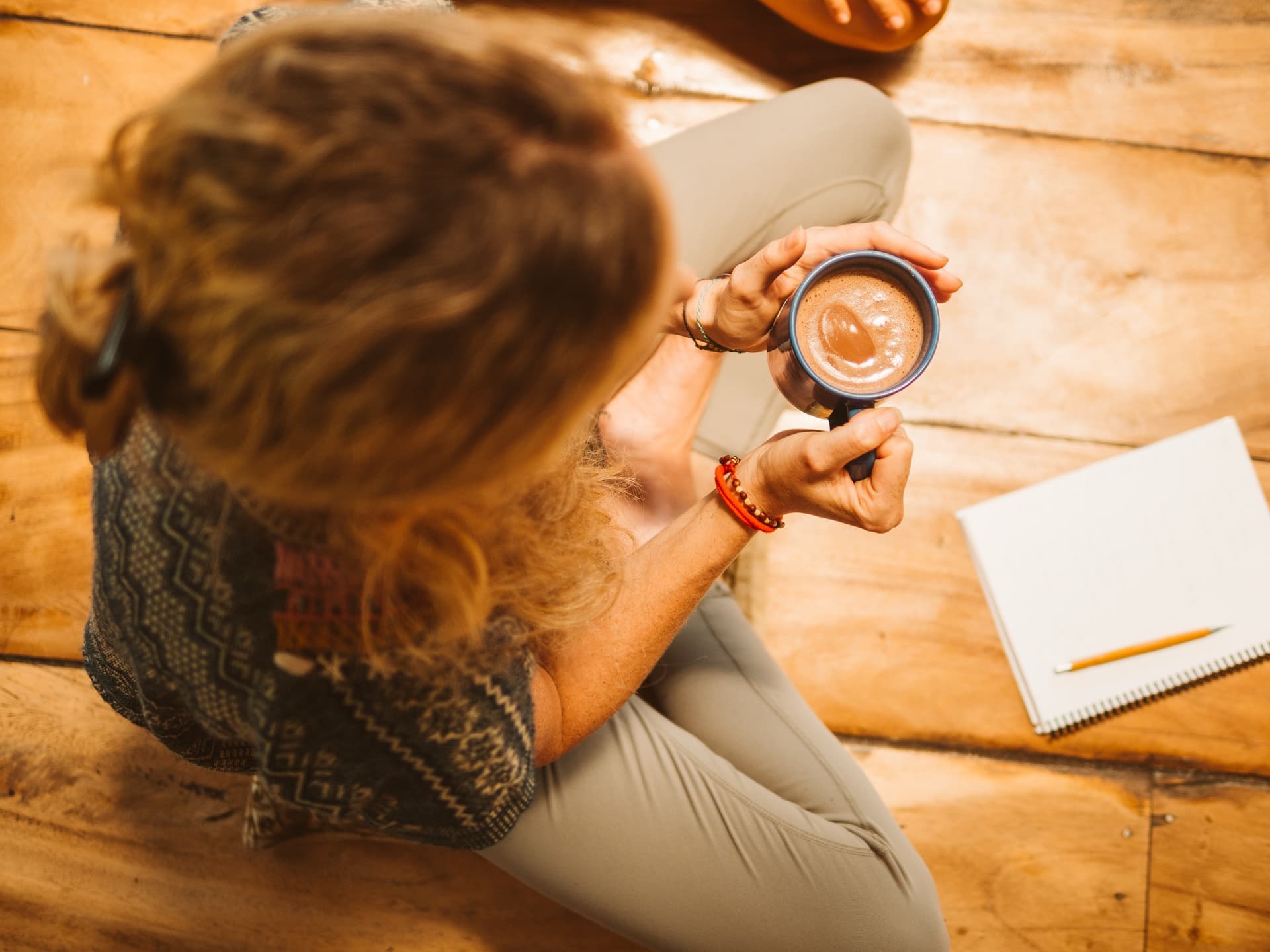 Ceremonial cacao in both hands, notebook open on the wooden floor