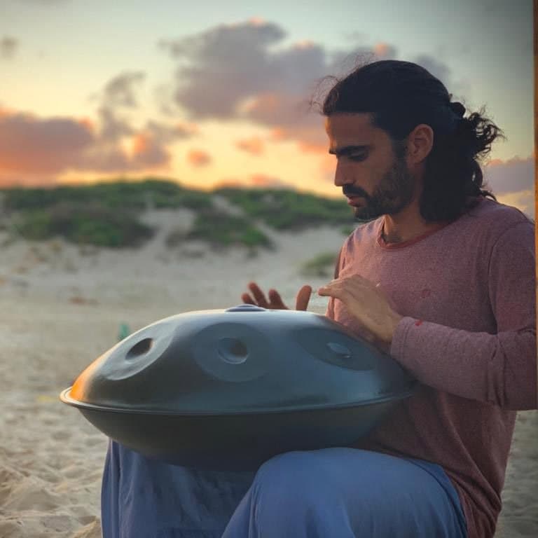 Eyal, a HeartSong Mastery student, playing a handpan on the beach at sunset
