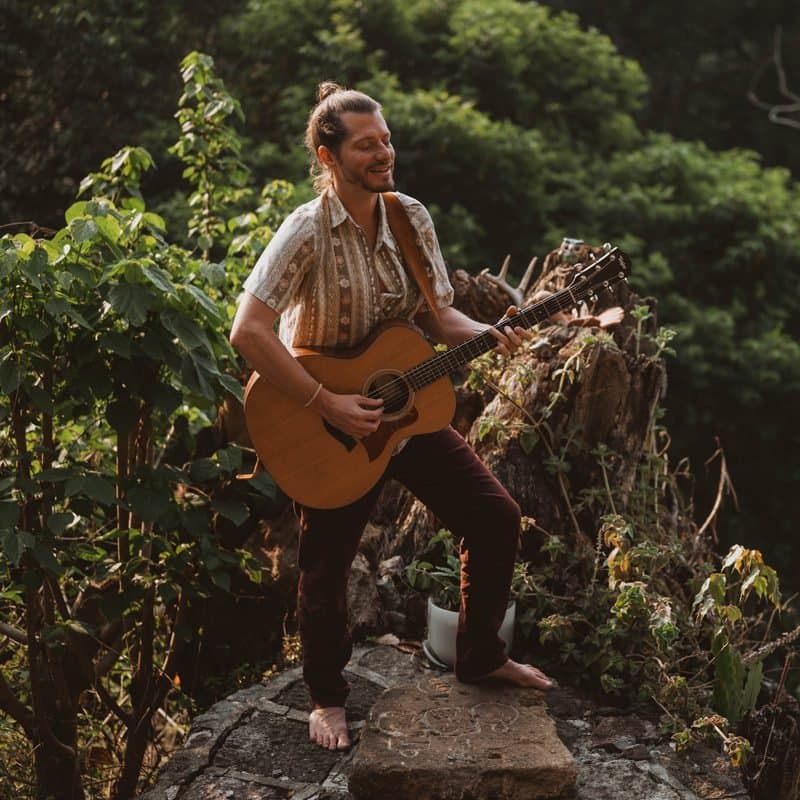 Matt, a HeartSong Mastery student, playing guitar barefoot on a stone altar in the jungle