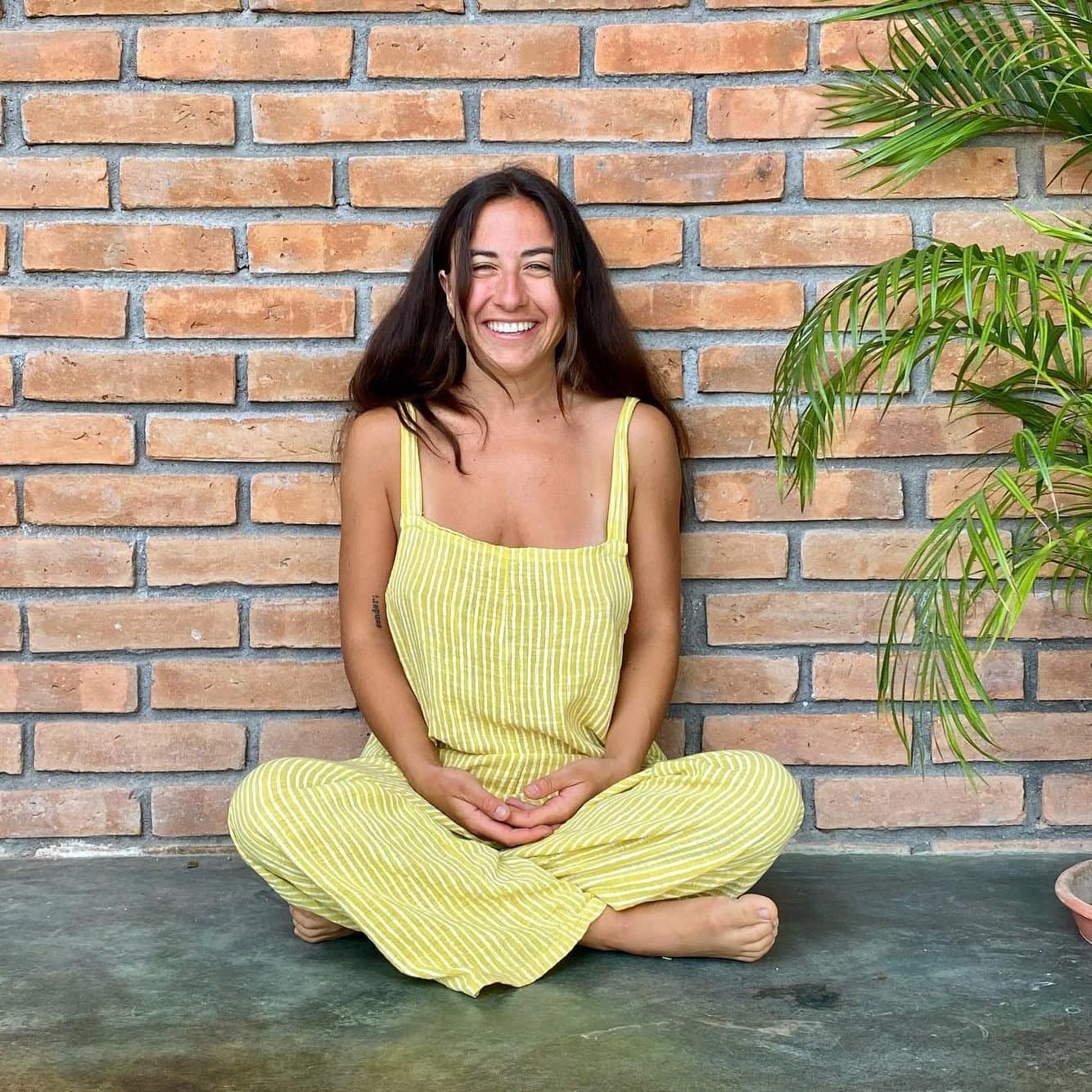 Rhiannon, a HeartSong Mastery student, smiling cross-legged against a brick wall